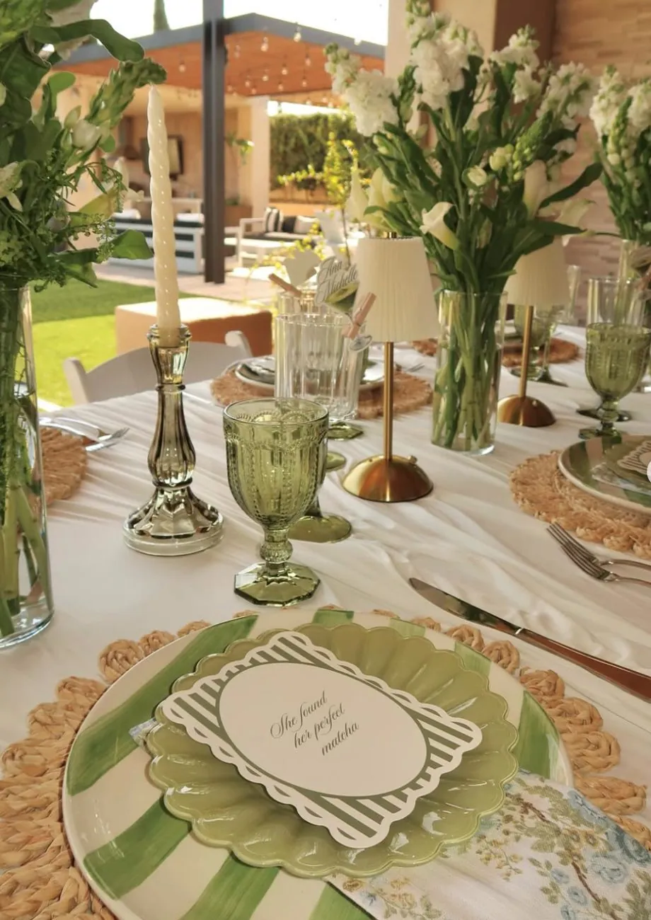 Green and white place setting with rattan charger, candles and white florals